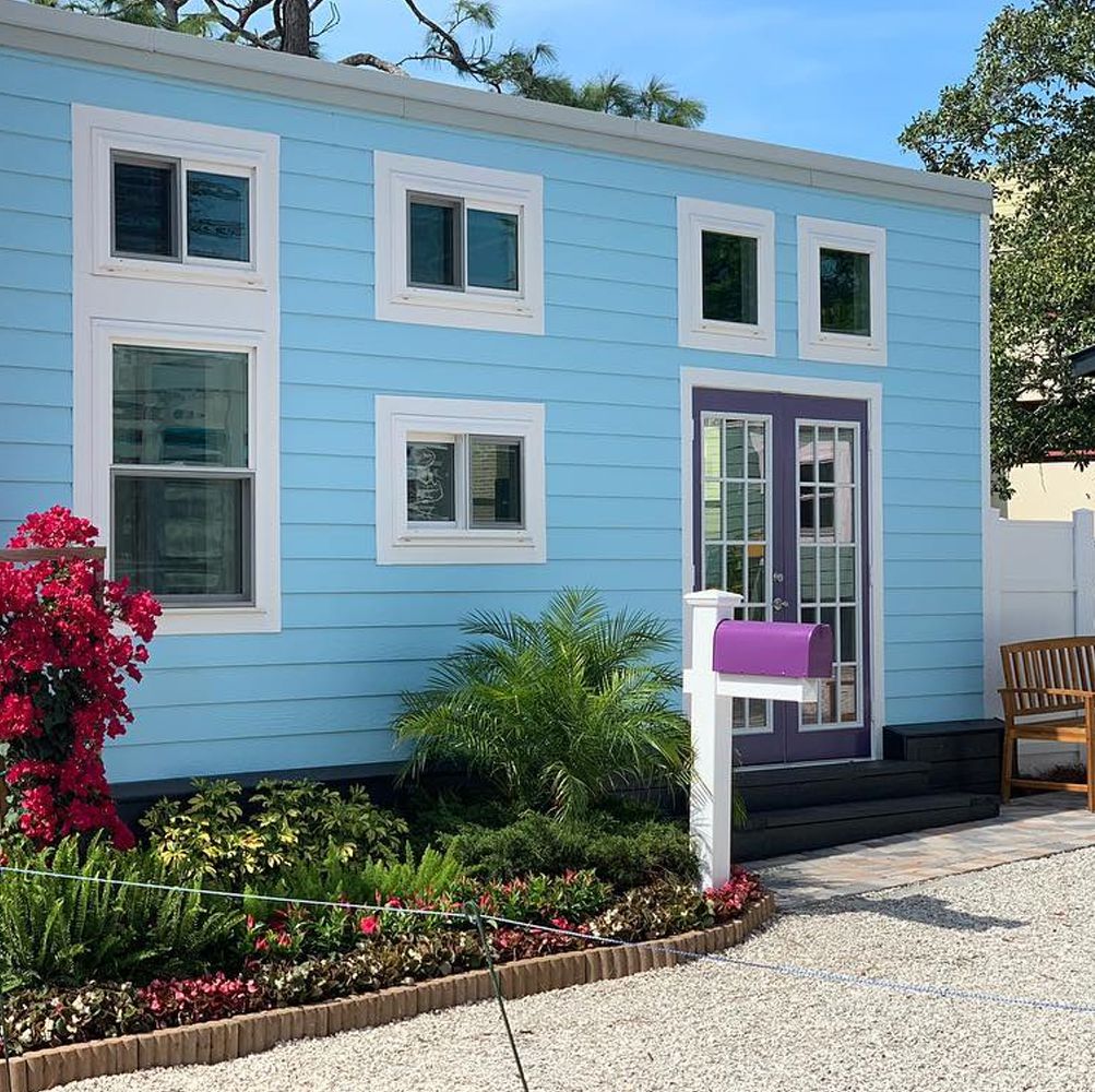 Light blue tiny cottage with white trim, glass double doors, a mailbox and tropical landscaping out front