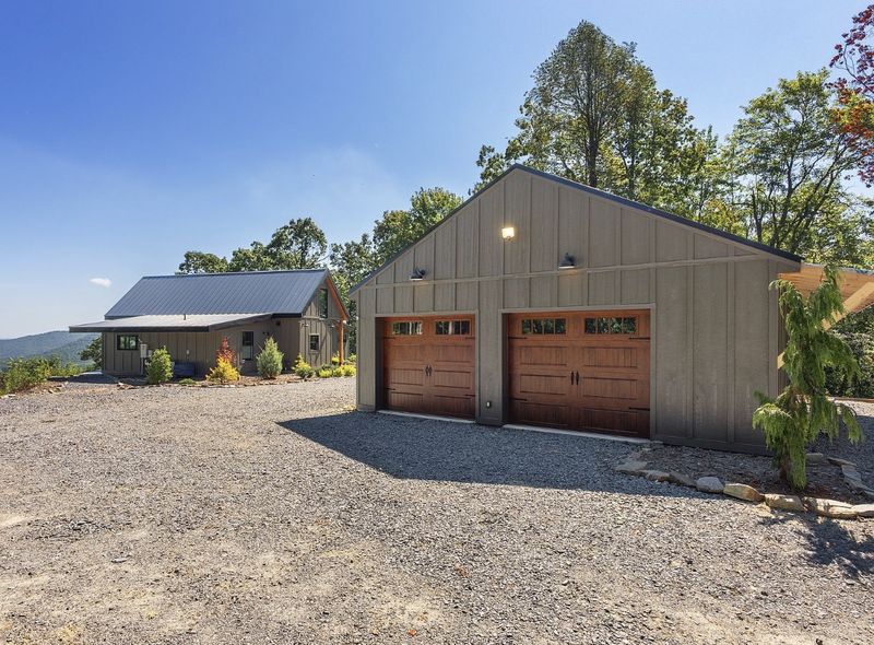 Detached two-car garage with wood-look doors next to the main house on a gravel drive, with mountains behind