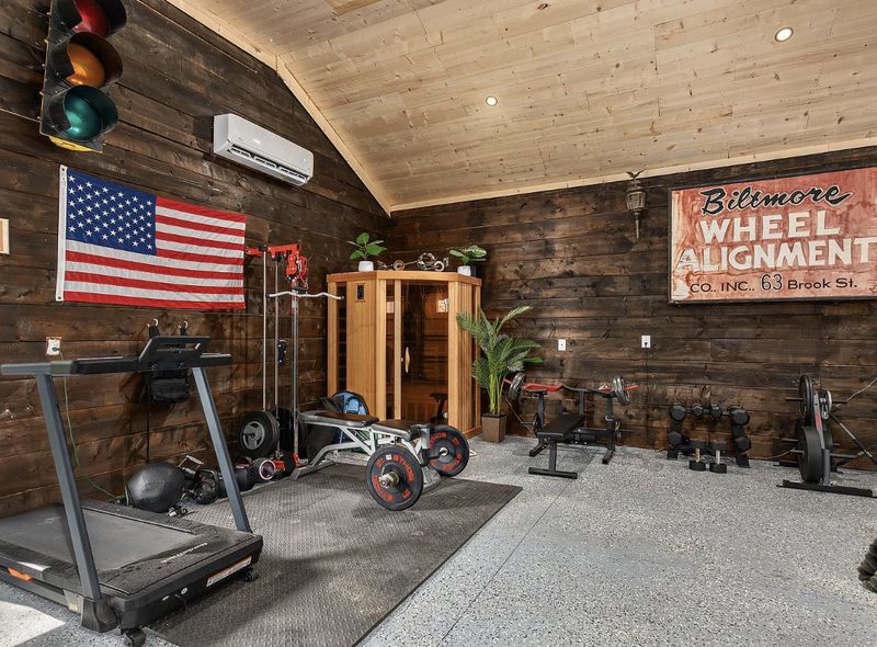 Wood-paneled garage gym with a treadmill, cable machine, free weights and a corner infrared sauna