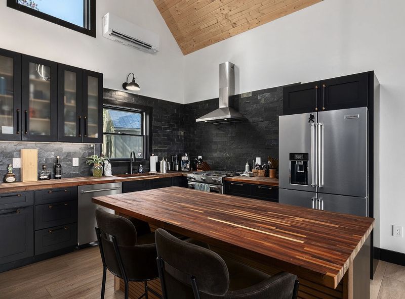 Kitchen with black shaker cabinets, a black slate backsplash, a walnut butcher-block island, stainless range and a wall-mounted mini-split