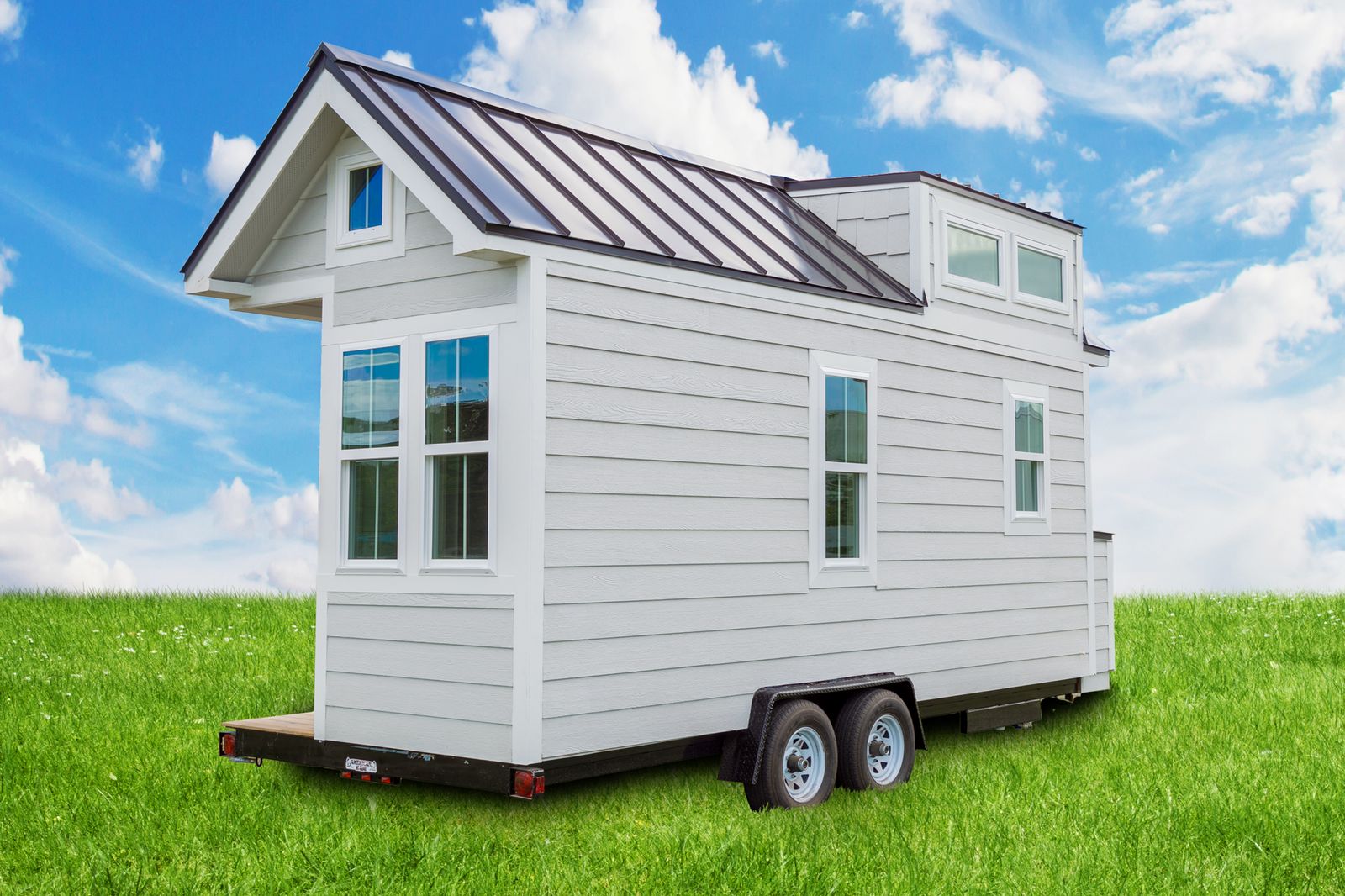 Gray lap-sided tiny house with a standing-seam metal roof and dormer, on a tandem-axle trailer