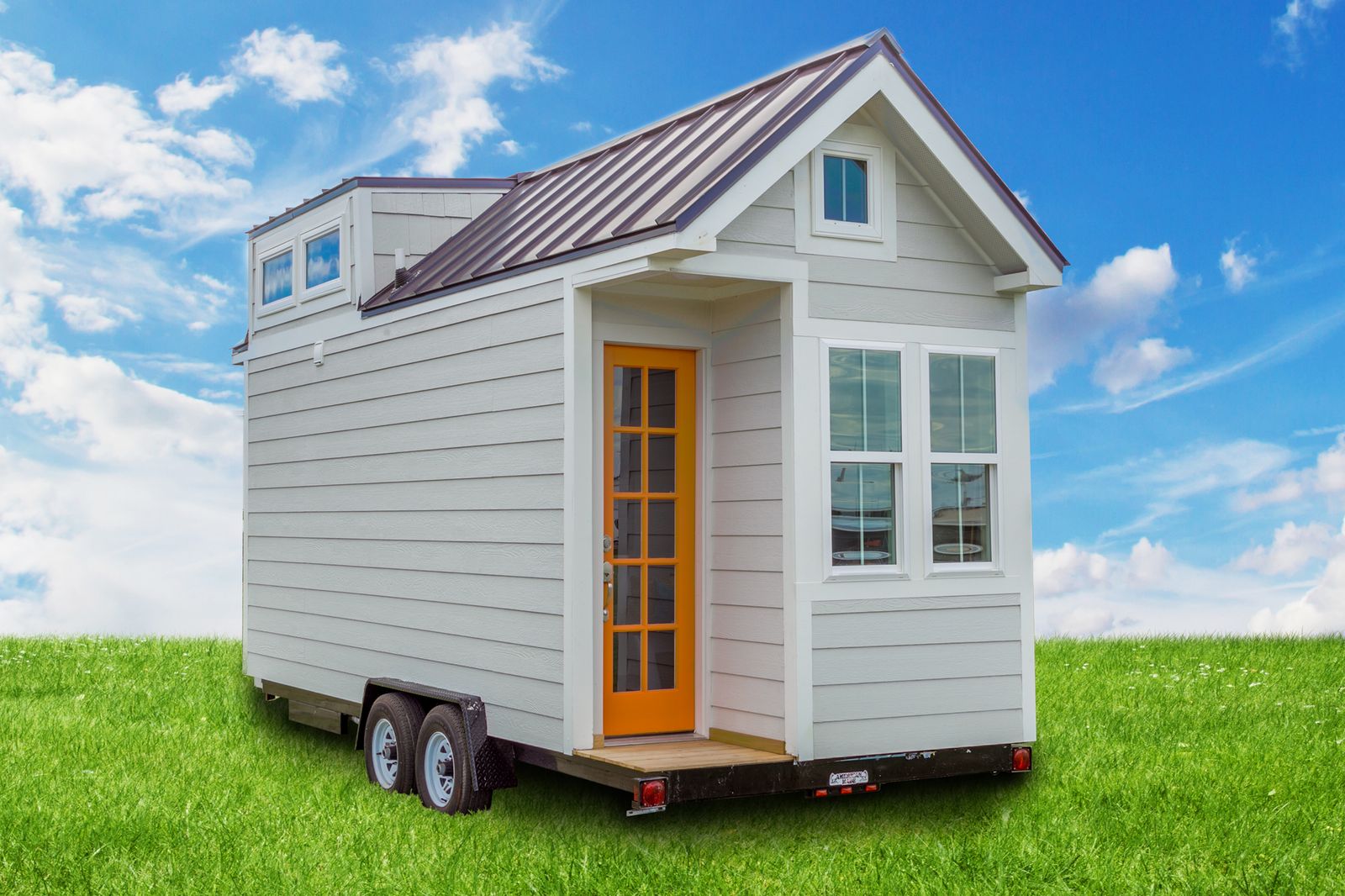 White tiny house on wheels with lap siding, an orange glass-panel door, a standing-seam metal roof and a tandem-axle trailer