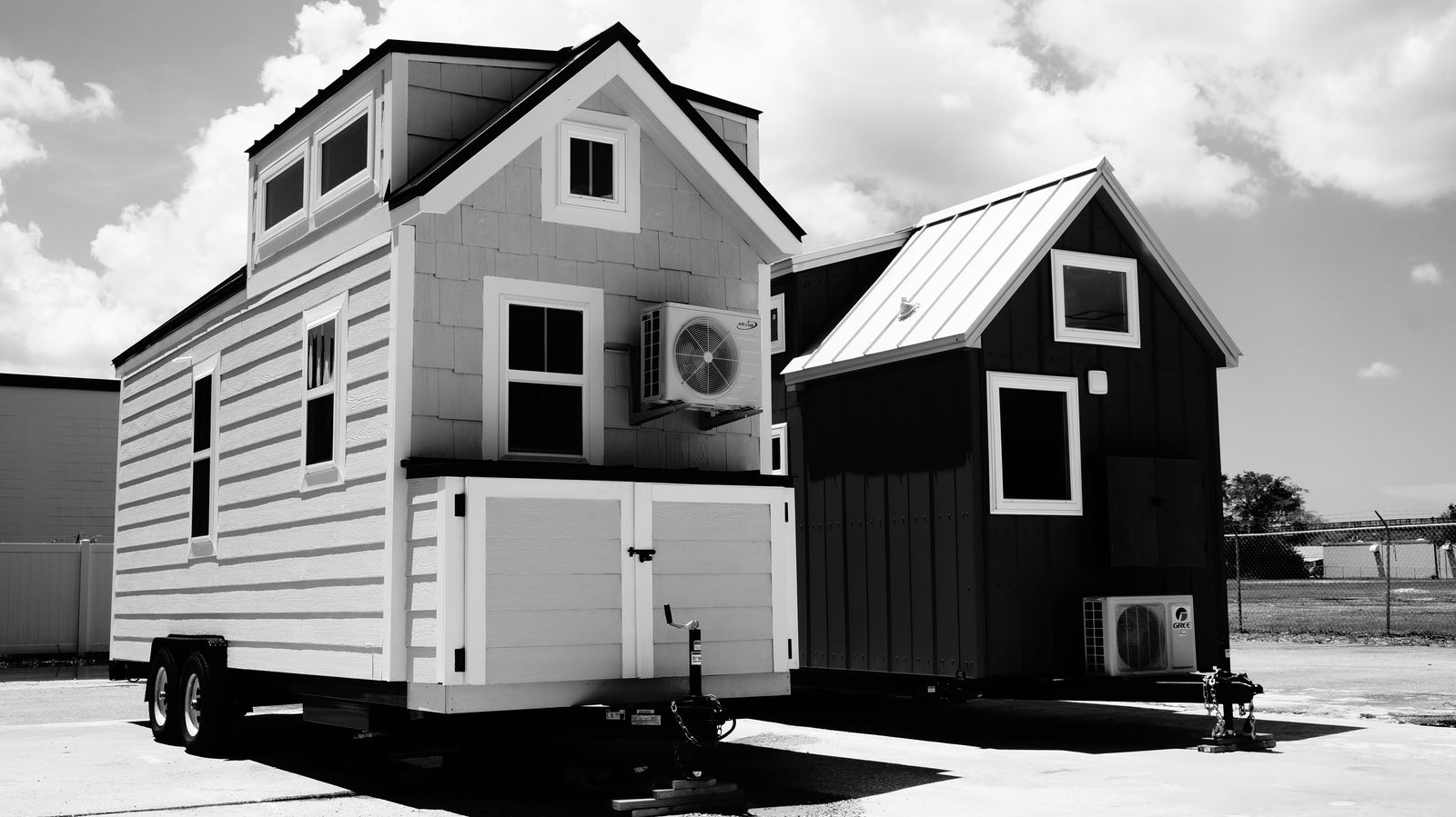 Two tiny houses on wheels side by side, each with a wall-mounted mini-split condenser